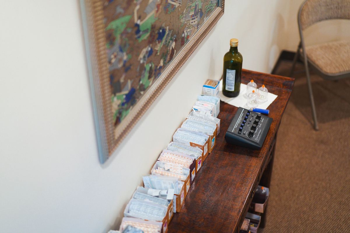 Acupuncture treatment room sideboard at Integrative Health Partners — multiple gauge needle boxes, electroacupuncture stimulator, glass cupping cups, and clinical Chinese painting