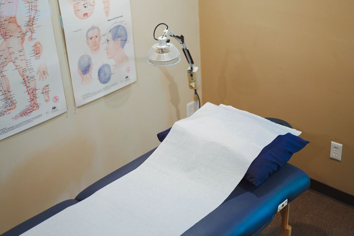 Acupuncture treatment table at IHP Greenville with TDP heat lamp and head, face and scalp acupuncture point charts — professional clinical setting