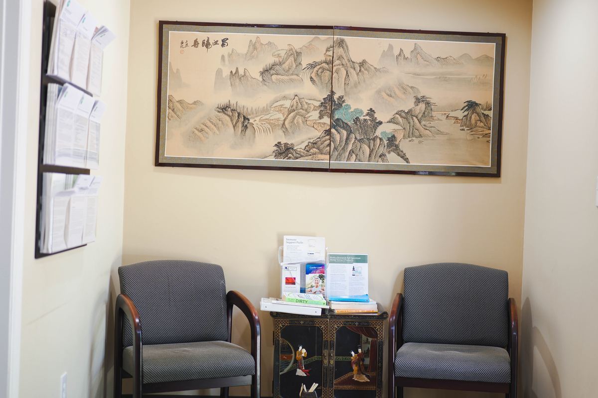 Waiting area at Integrative Health Partners Greenville SC — two chairs beneath a large traditional Chinese mountain landscape painting, with health resource table